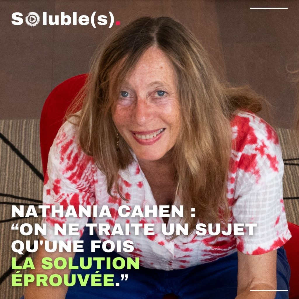 Portrait de Nathania Cahen, souriante, chemisier blan aux motifs rouge, assise dans un fauteil rouge.. Citation sur l'image : “ON NE TRAITE UN SUJET QU'UNE FOIS LA SOLUTION ÉPROUVÉE.” NATHANIA CAHEN :