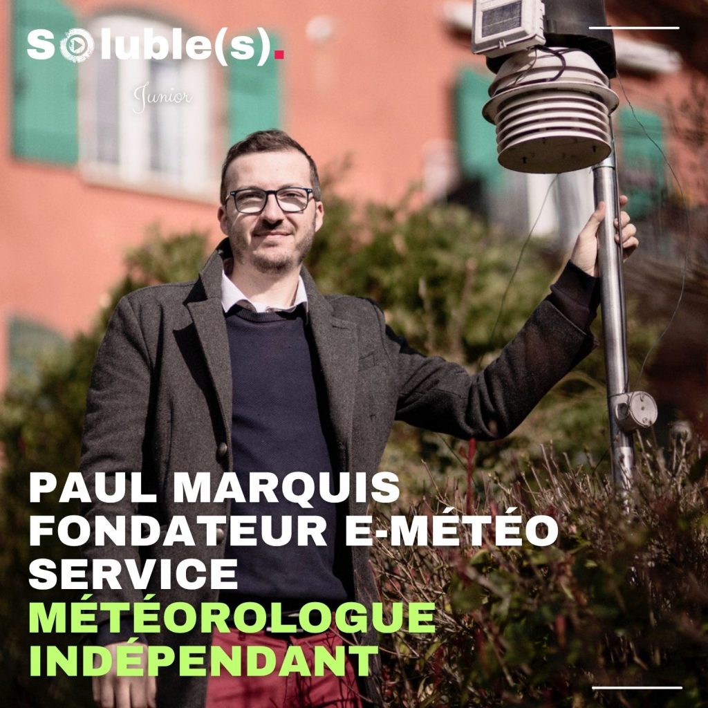 Portrait de Paul Marquis, fondateur d’E-meteo Service et météorologue indépendant, posant à l’extérieur devant une station météo, sur fond de bâtiment coloré.
