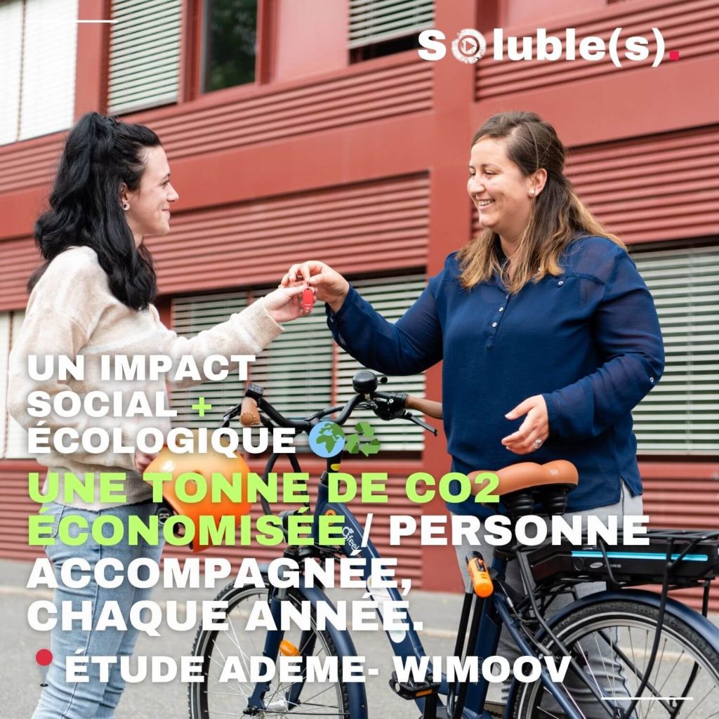 Deux femmes échangent des clés devant un vélo, symbole d’entraide. Texte à lire : « Un impact social + écologique 🌍🌳 Une tonne de CO2 économisée par personne accompagnée, chaque année. - Étude Ademe-Wimoov »