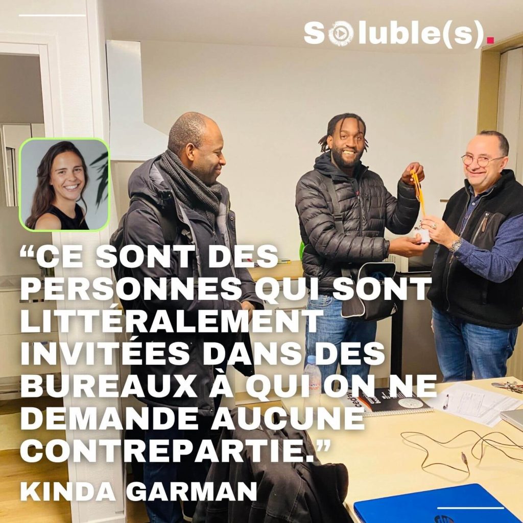 Scène de vie solidaire montrant trois hommes souriants échangeant dans une cuisine de bureau, avec une citation de Kinda Garman : "Ce sont des personnes qui sont littéralement invitées dans des bureaux à qui on ne demande aucune contrepartie".